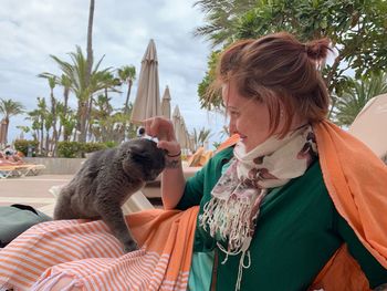 Smiling woman stroking cat against sky