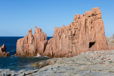 Rock formations in sea against clear blue sky