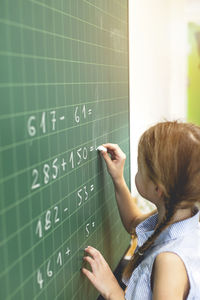 Girl solving mathematics equation on blackboard in classroom at school