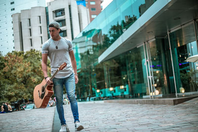 Full length of young man with guitar walking on street in city
