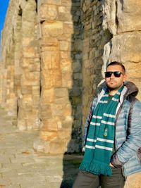 Man wearing sunglasses standing against stone wall