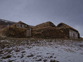 Abandoned house on snow covered field against sky