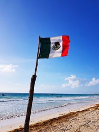 Mexican flag on beach against blue sky