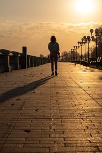 Rear view of silhouette people walking on boardwalk during sunset