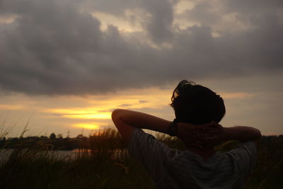 Rear view of woman on field against sky during sunset