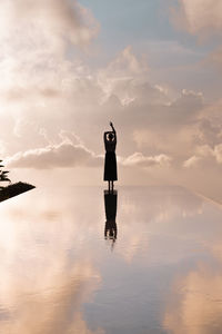 Silhouette woman standing on infinity pool against sky during sunset