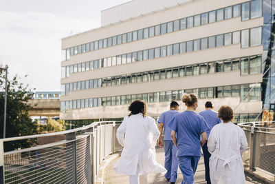 Male and female healthcare professional walking on bridge leading towards hospital