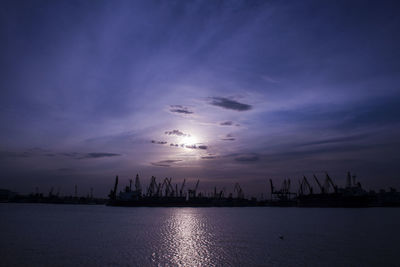 Silhouette of cranes at commercial dock against sky during sunset