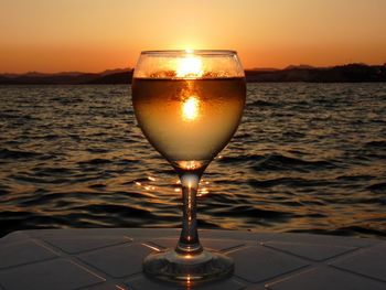 Close-up of wineglass against sea during sunset