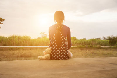 Rear view of woman sitting on field against sky