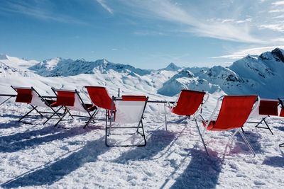 Empty chairs on snow covered mountain against sky