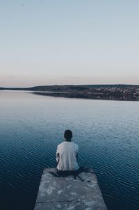 Rear view of man sitting on sea against clear sky