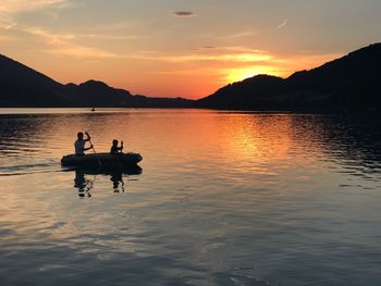 Silhouette men in lake against sky during sunset