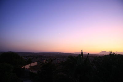 Silhouette trees and cityscape against sky during sunset