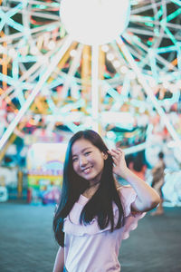 Portrait of smiling young woman standing at amusement park during night