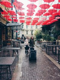 Portrait of woman with friend holding luggage below red umbrellas