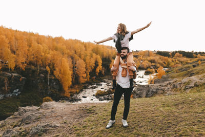 Full length of young man with arms raised against sky