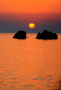 Silhouette rocks in sea against sky during sunset