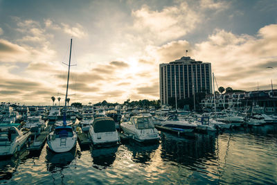 Boats moored at harbor against cloudy sky during sunset