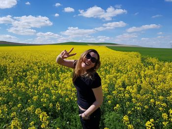 Portrait of happy mid adult woman wearing sunglasses while standing amidst flowers against sky during sunny day