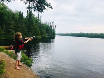 Boy fishing while standing by lake