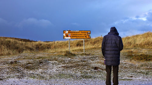 Rear view of man standing on field against sky