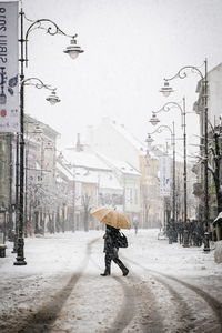 Rear view of person walking on street amidst buildings during winter