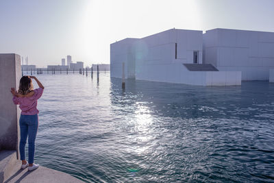 Full length rear view of woman shielding eyes while looking at building by river