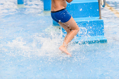 Low section of boy running in water by steps