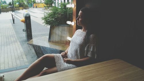 Side view of young woman sitting on table