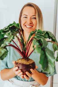 Young woman holding beetroots with green leaves and smiling at camera