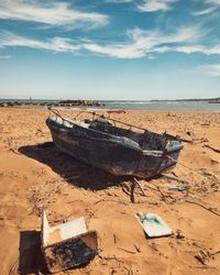Abandoned boat on sand at beach against sky