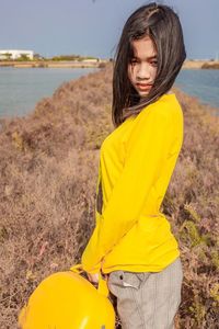 Portrait of beautiful women standing in a filed with yellow travel bag.