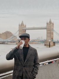 Man drinking coffee while standing against bridge