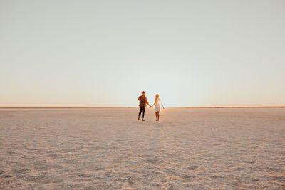 Rear view of woman walking at beach against clear sky