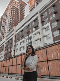 Portrait of young woman standing against buildings in city