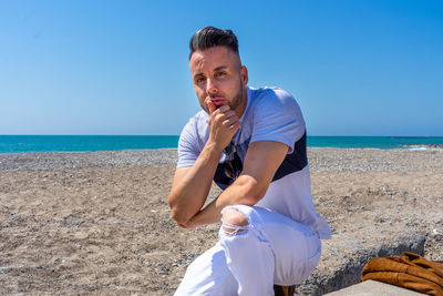 Portrait of man sitting on beach against clear blue sky