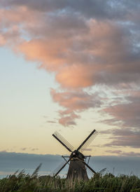 Traditional windmill on field against sky during sunset