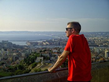 Side view of man looking at cityscape against sky