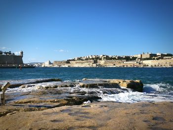 View of sea and buildings against clear blue sky