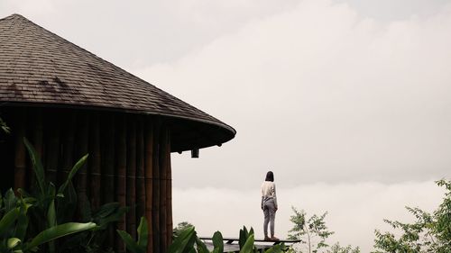 Rear view full length of woman standing by hut against sky