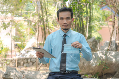 Portrait of young man holding surgical mask outdoors