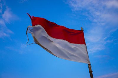 Low angle view of torn flag against blue sky