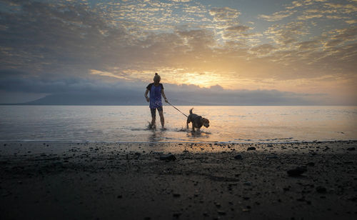 Woman with dog on beach during sunset