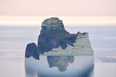 Digital composite image of rock formation in sea against sky during sunset