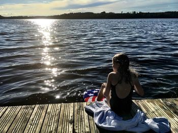 Rear view of man sitting on bench by lake