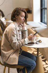 Young woman using mobile phone while sitting on table