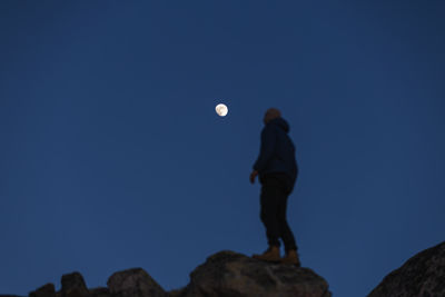 Low angle view of man standing on rock against clear sky