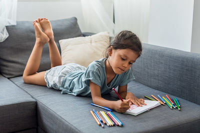 Hispanic girl painting on a sofa with pencil colors.