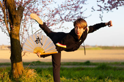 Young caucasian woman posing a wushu martial art posture in a sunny day, a pink tree in background